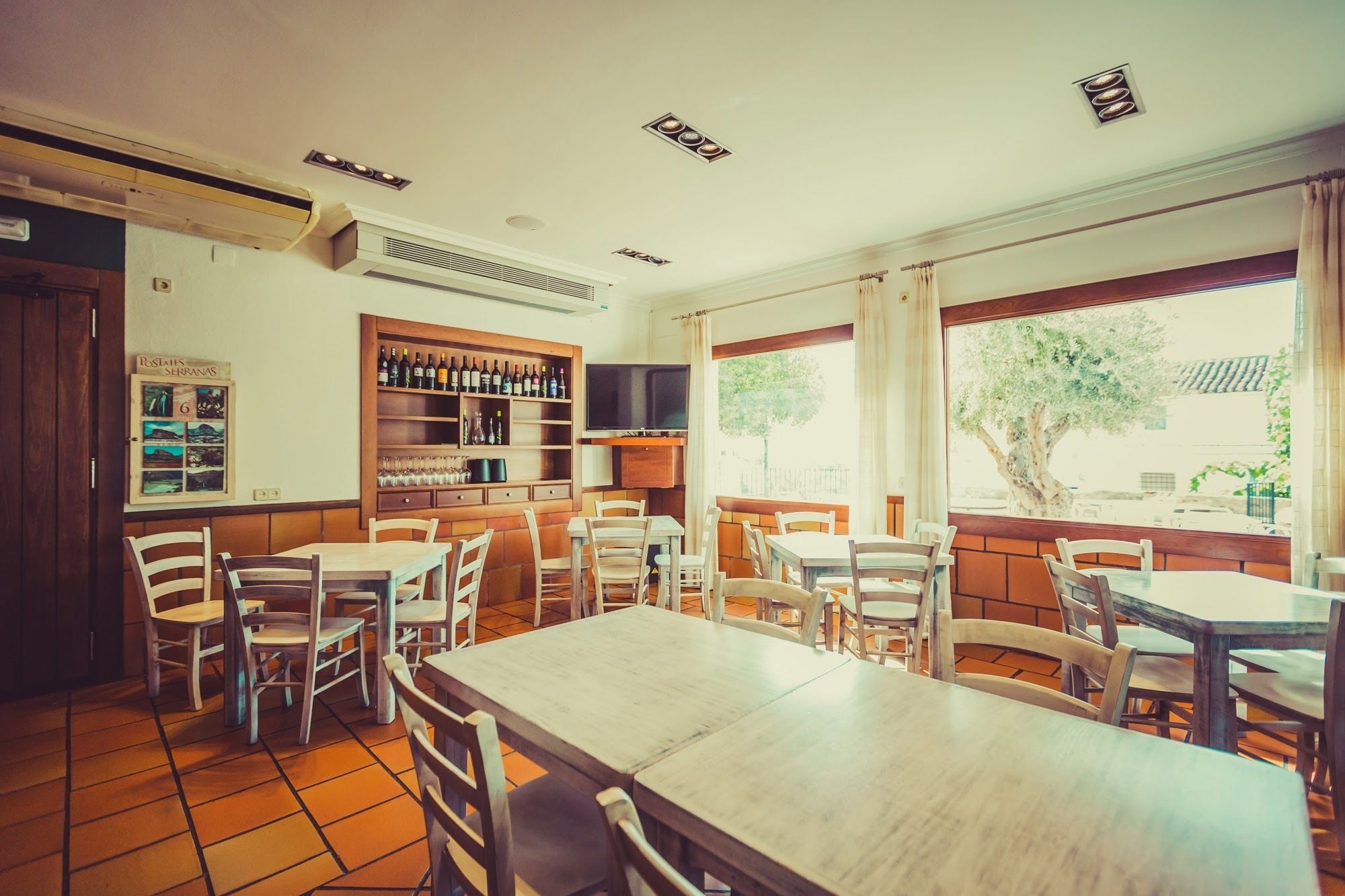 Un restaurant amb taules i cadires de fusta, una prestatgeria de vi i una pantalla de televisió.