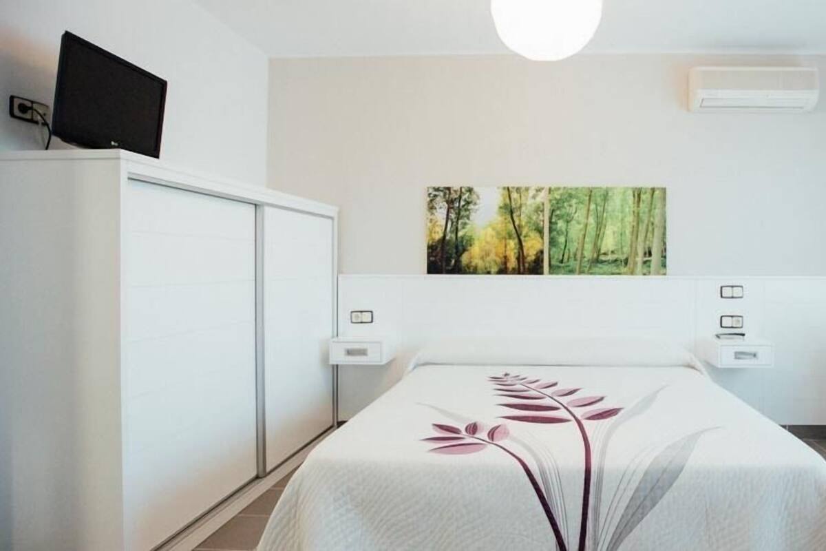 Een moderne hotelkamer met een bed, een bureau en een stoel. Er hangt een schilderij aan de muur en er is een airconditioner.