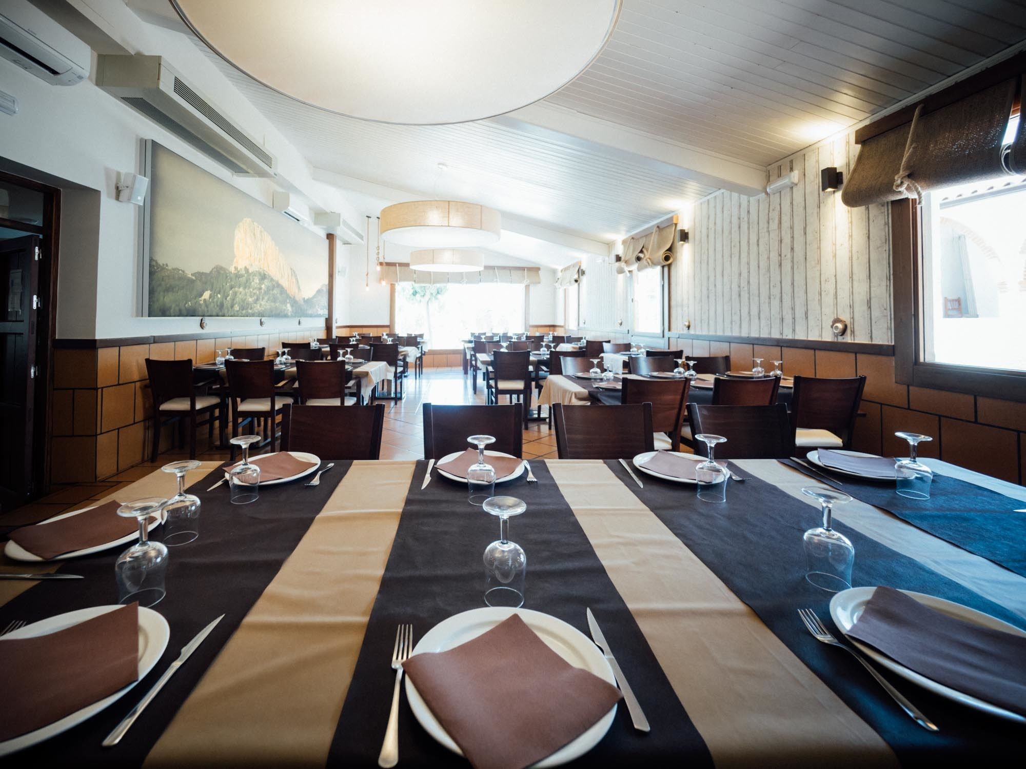 A restaurant with multiple tables set for dining, featuring a panoramic view of a mountainous landscape.