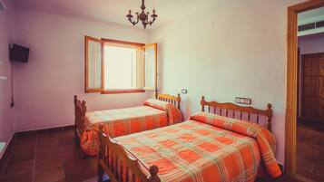 Un dormitorio con dos camas de madera, una araña, una ventana con cortinas y una puerta.