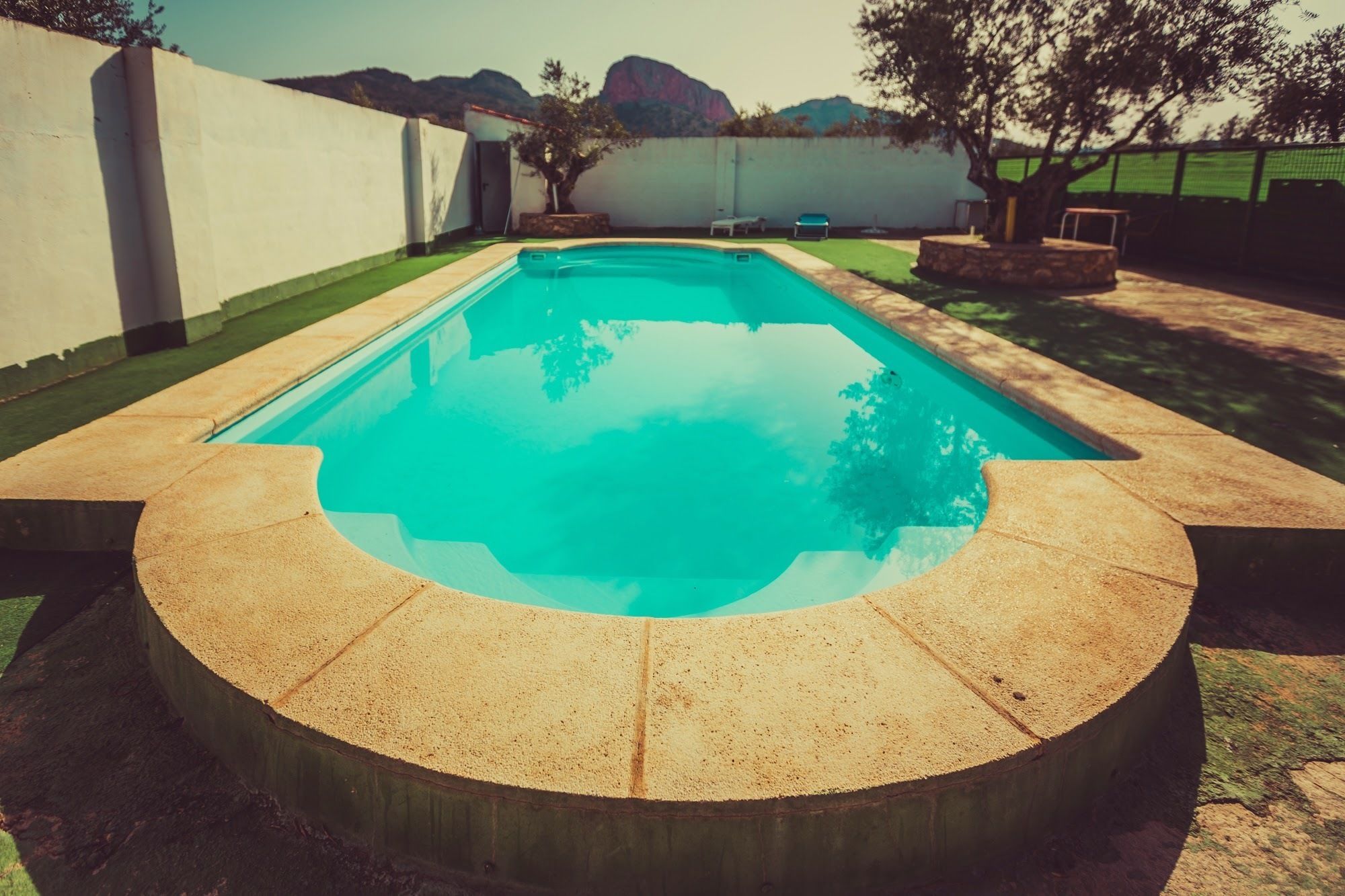 A rectangular swimming pool with a curved edge, surrounded by a concrete deck.