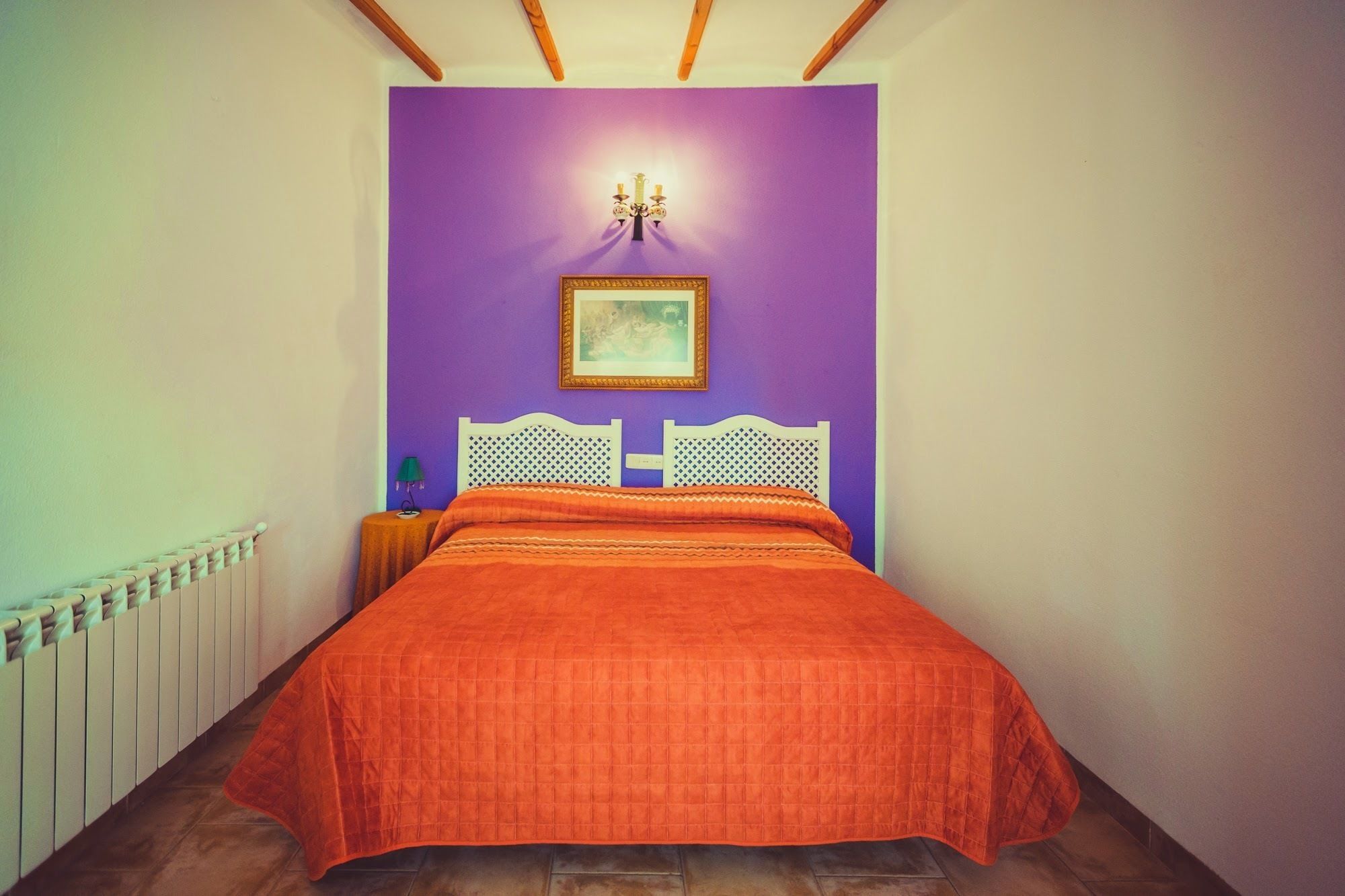 A bedroom with a purple wall, a white headboard, and a bed with an orange bedspread.