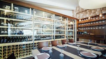 Un comedor con una mesa larga dispuesta para seis personas, rodeado de bodegueros y estanterías con botellas.