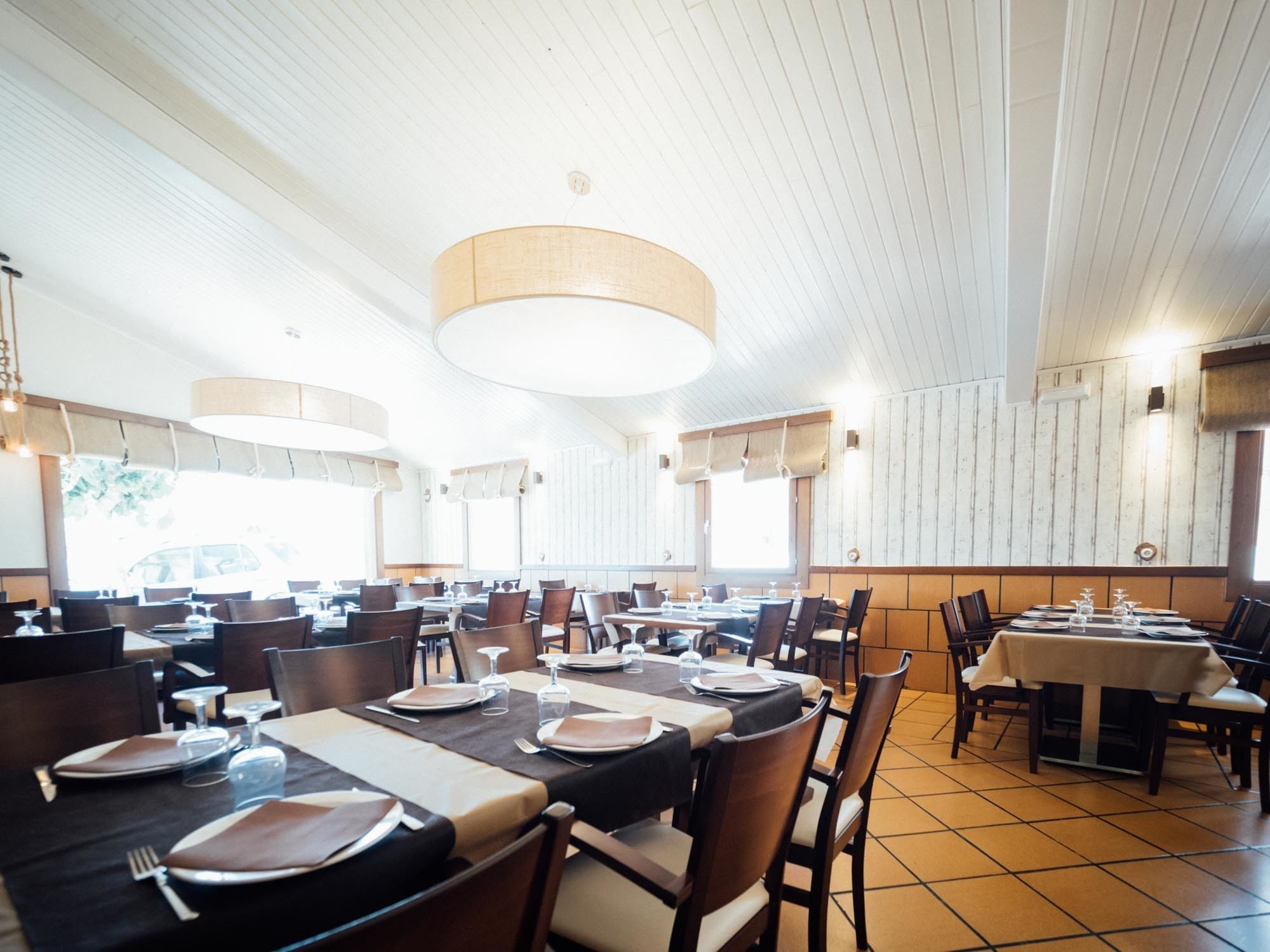 A restaurant with multiple tables set for dining, wooden panel walls, and hanging pendant lights.
