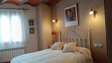 A bedroom with a bed, a window with curtains, a radiator, wall-mounted lights, and framed pictures.