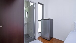 Una habitación de hotel con una cama, un pequeño espacio kitchenette, una puerta que da al baño y una ventana.