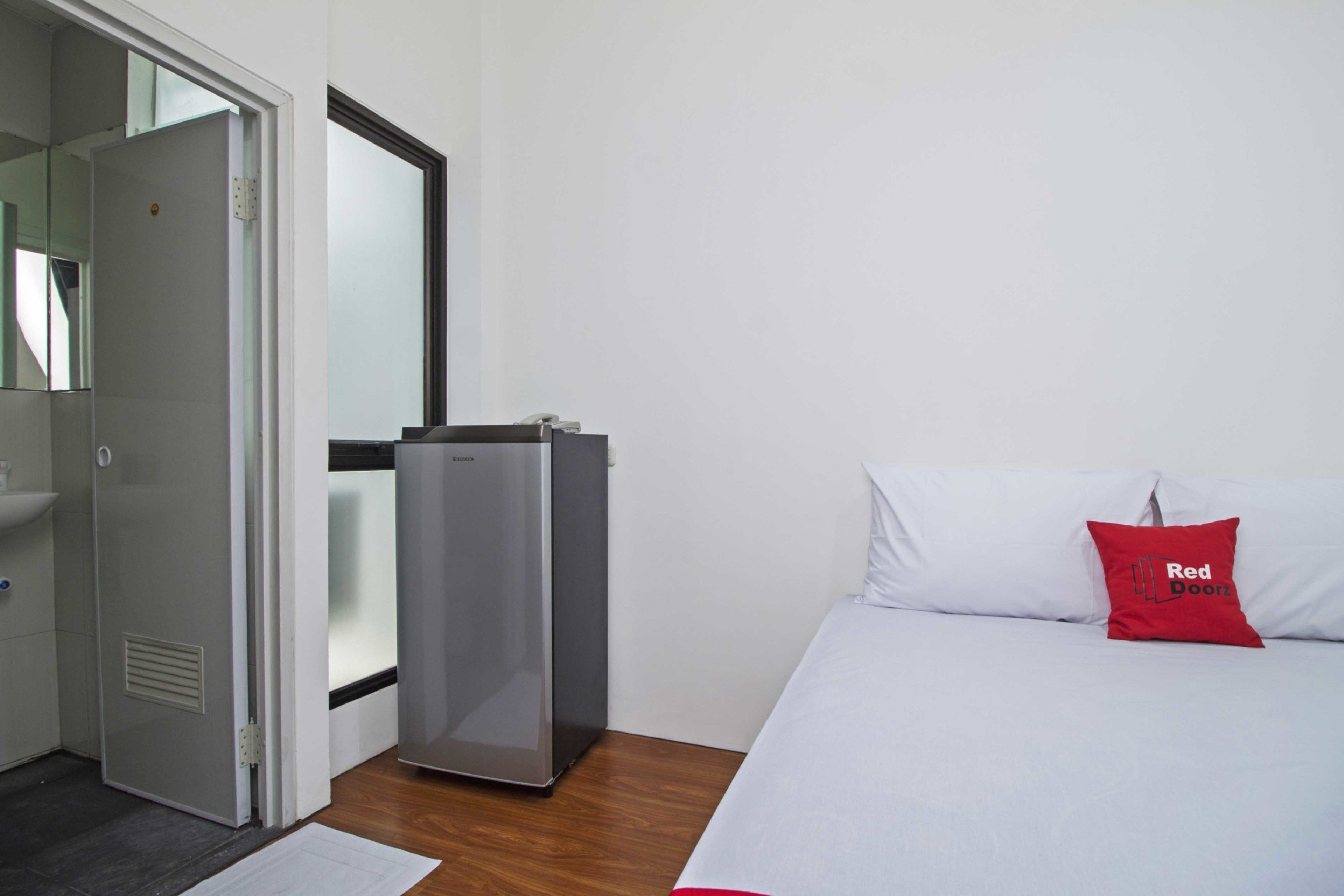 A hotel room with a bed, a small refrigerator, a door, and a mirror.