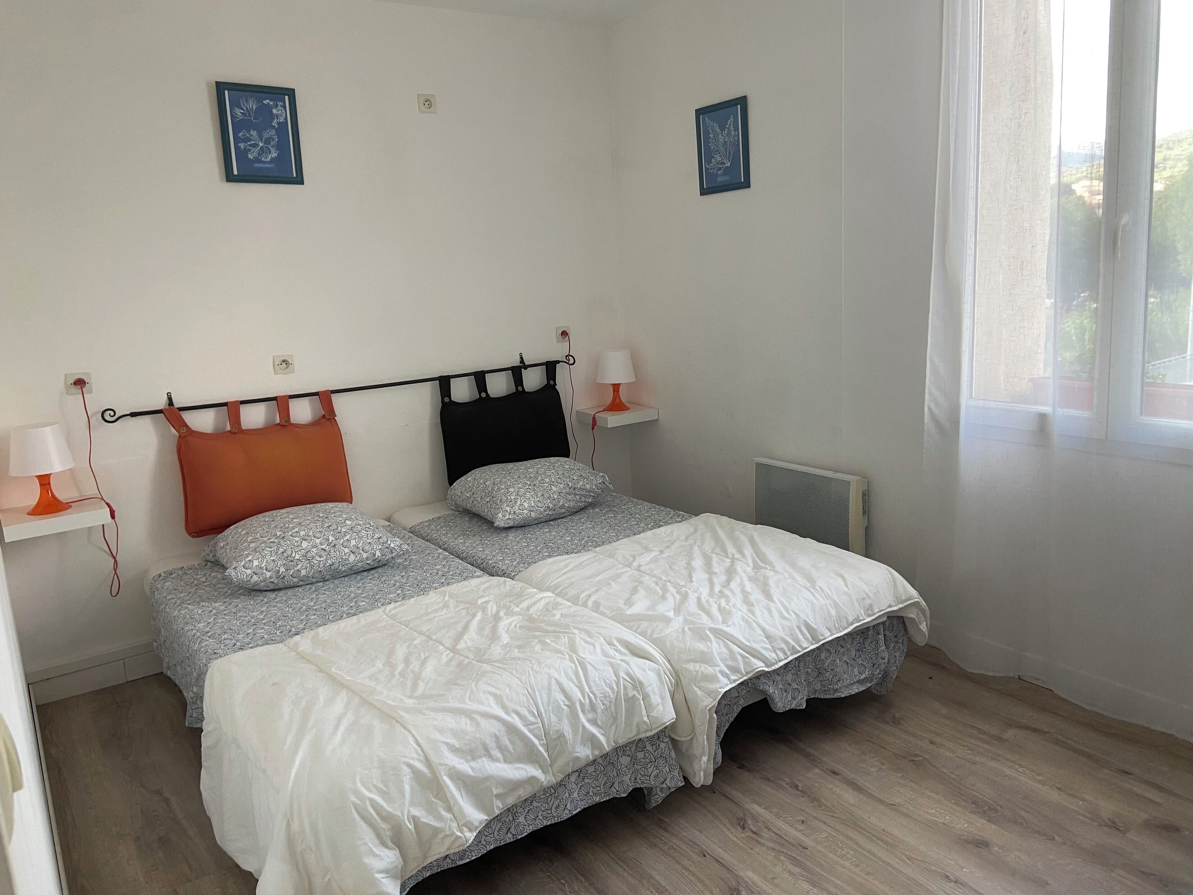 A bedroom with two beds, a radiator, and two wall-mounted lamps.