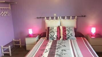 A bedroom with a bed, two bedside tables, a nightstand, a wall-mounted shelf, and a hanging rack.