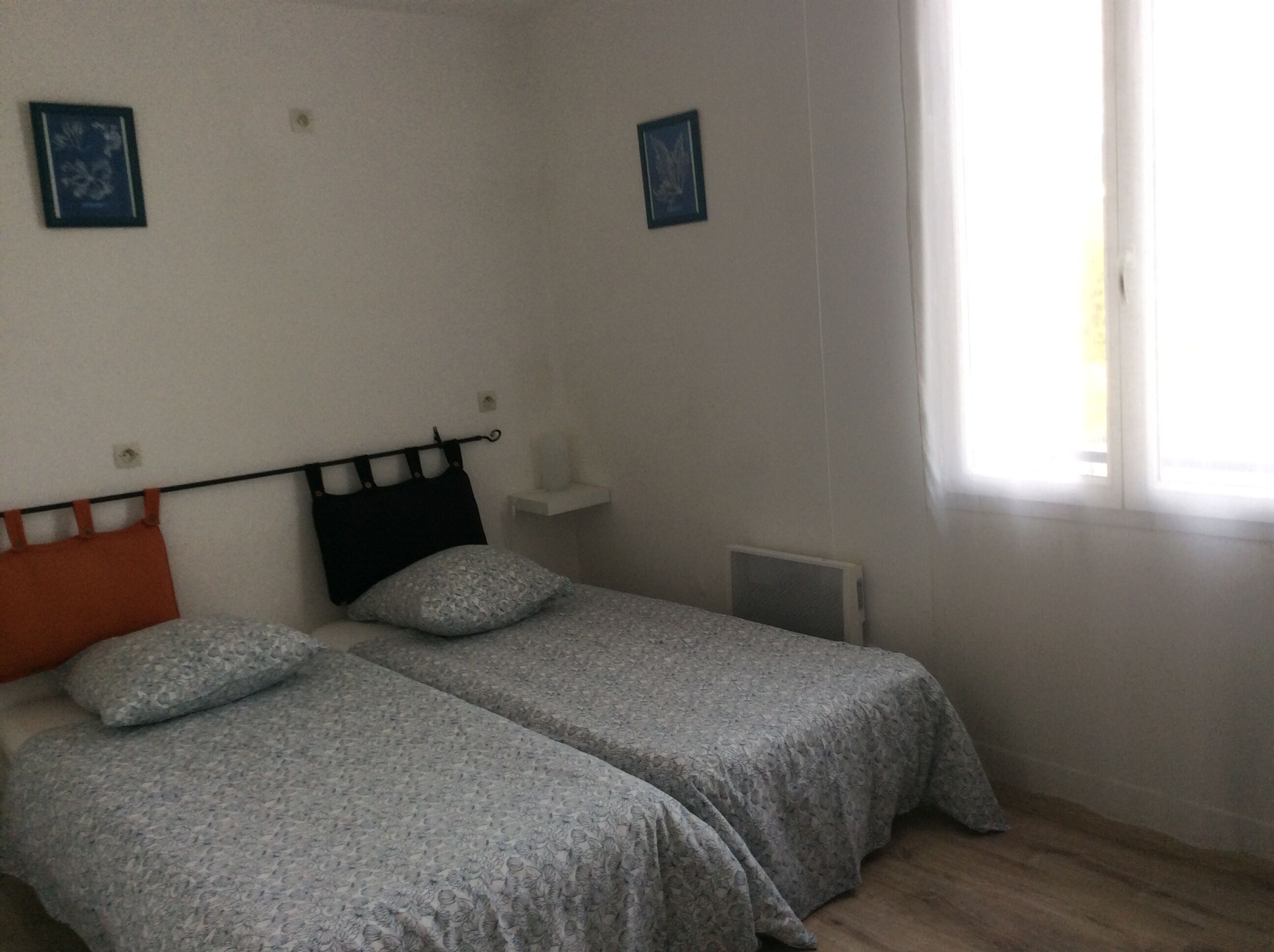 Een slaapkamer met twee eenpersoonsbedden, een radiator en een raam met gordijnen.