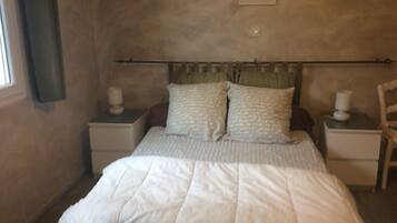 A bedroom with a bed, two bedside tables, a nightstand, a wall-mounted lamp, and a window with curtains.