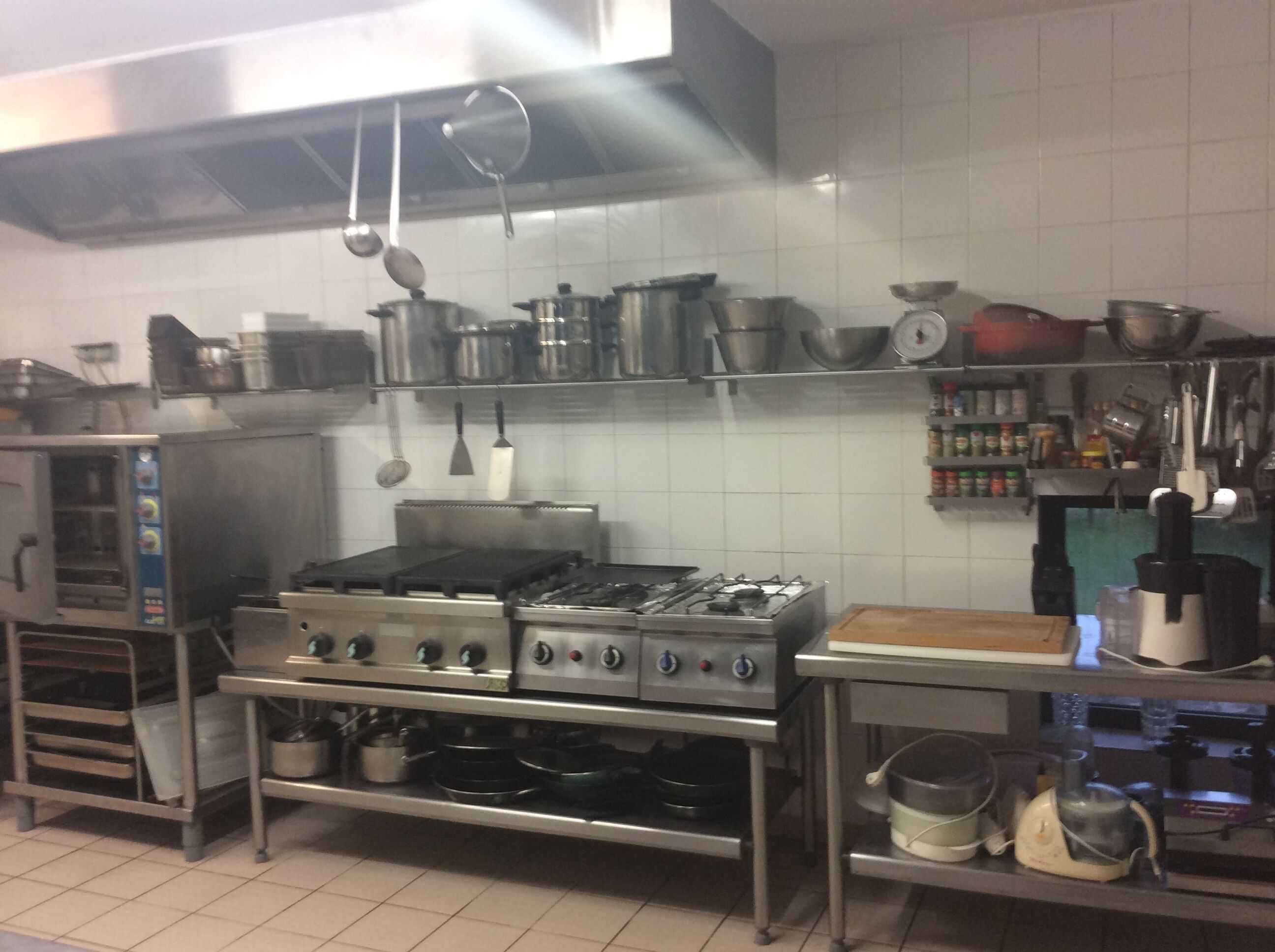 Eine gewerbliche Küche mit Edelstahlgeräten, darunter ein Herd, Töpfe und ein Mixer.