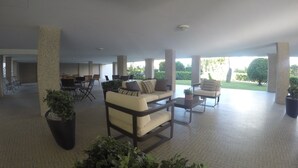 A spacious indoor area with a seating arrangement including a sofa and chairs, surrounded by large pillars and potted plants. - Residence Zenith (Caorle)