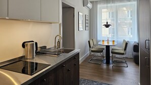 A modern kitchen with a built-in induction cooktop, a kettle, and a coffee machine. There is a dining area with a round table and two chairs. - Wine Apartments (Kraków)