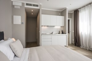 A modern hotel room with a bed, a kitchenette, and a bathroom.