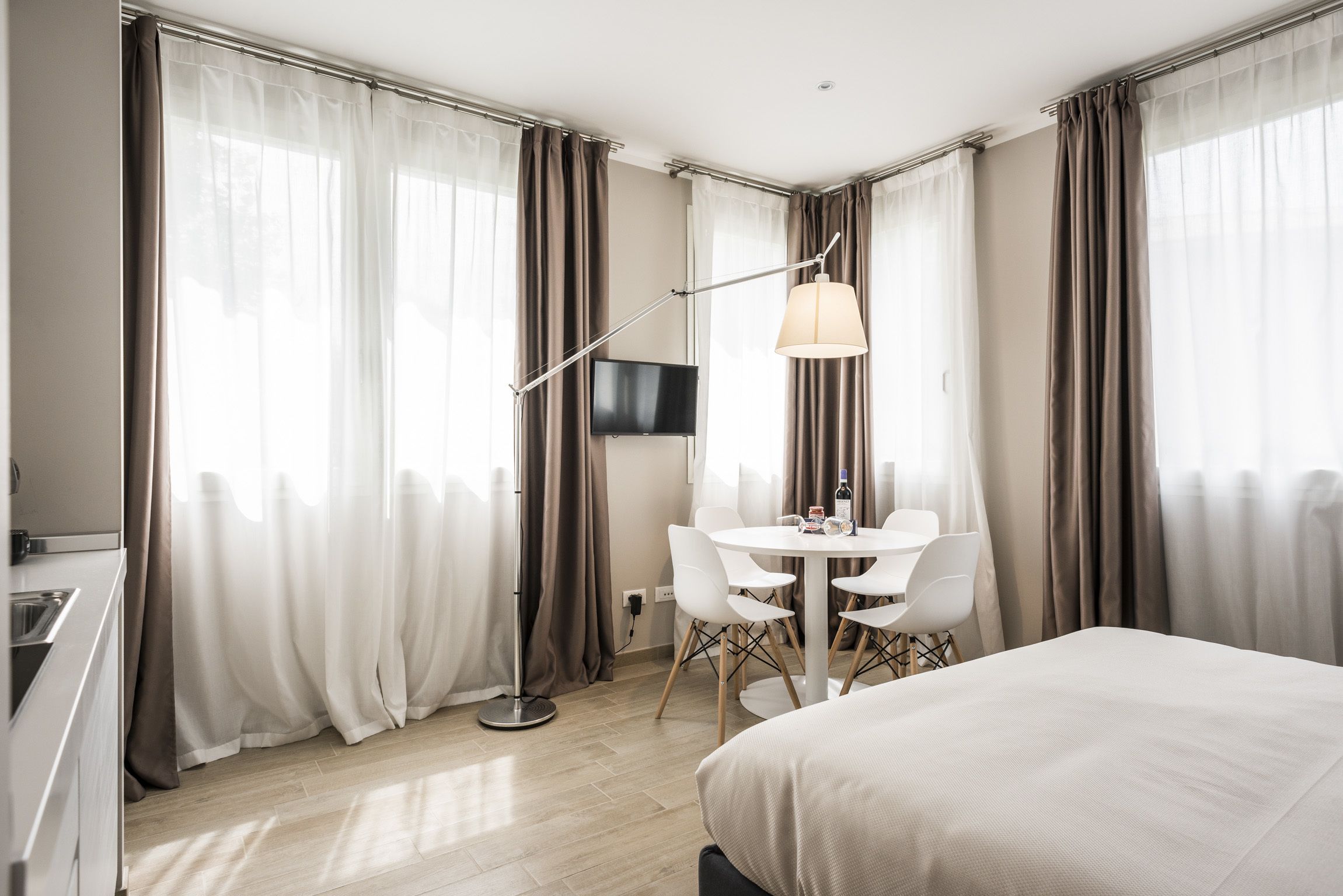 A hotel room with a bed, a desk, a chair, a table, a TV, and curtains.