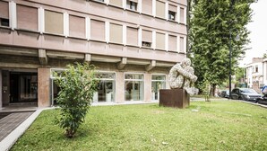 A building with a modern facade, a grassy area with a sculpture, and a tree. - MYSWEETPLACE - Largo Europa Apartments (Padova)