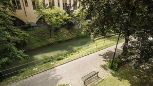 A paved walkway alongside a river with a bench and greenery. - MYSWEETPLACE - Largo Europa Apartments (Padova)
