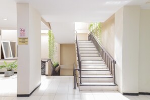A clean, modern indoor staircase with metal railings, surrounded by white walls and tiled floors. - RedDoorz near Gubeng Station (Surabaya)