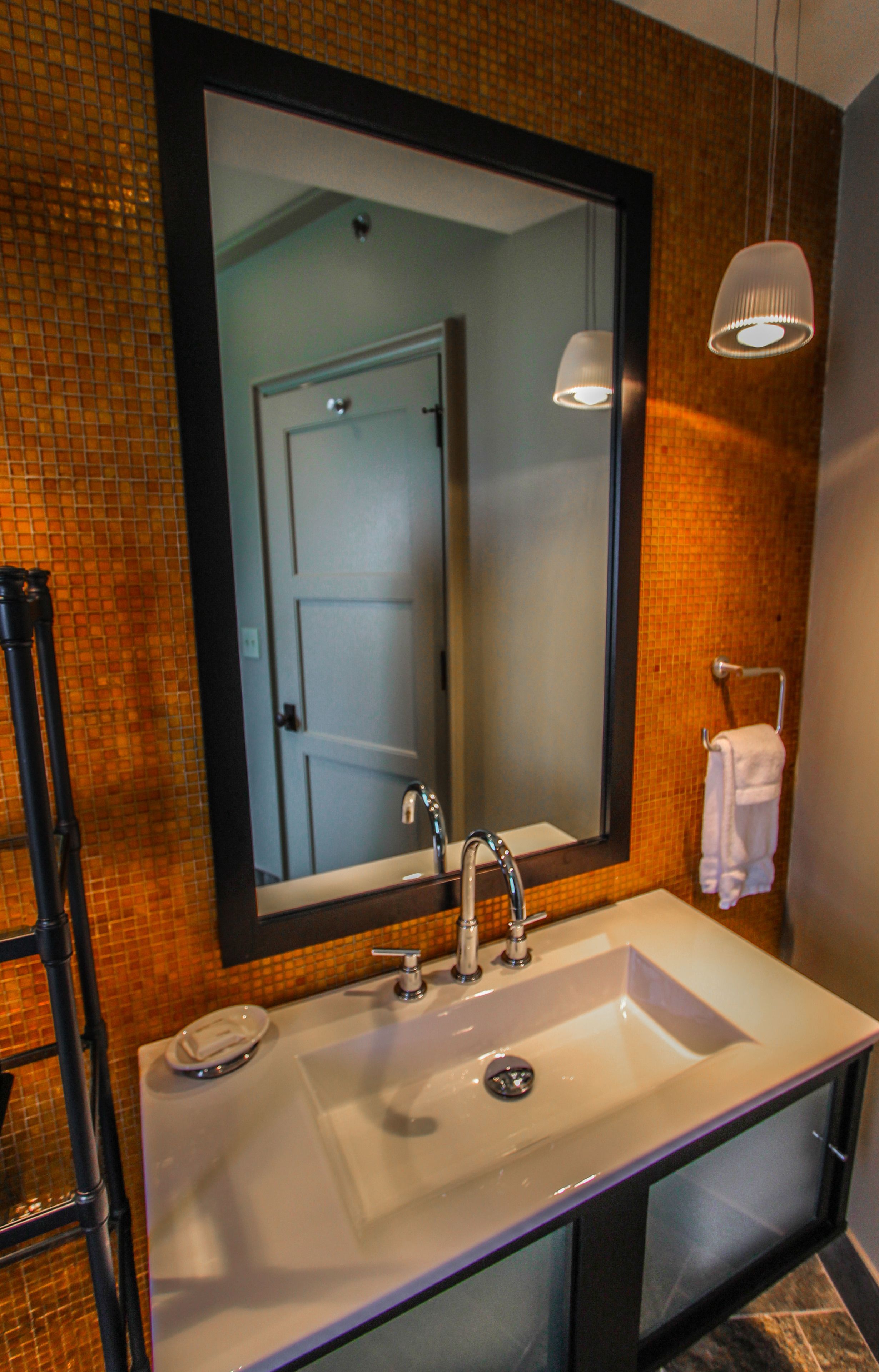 Un bagno con uno specchio grande, un lavandino bianco, un porta asciugamani e una lampada a sospensione.