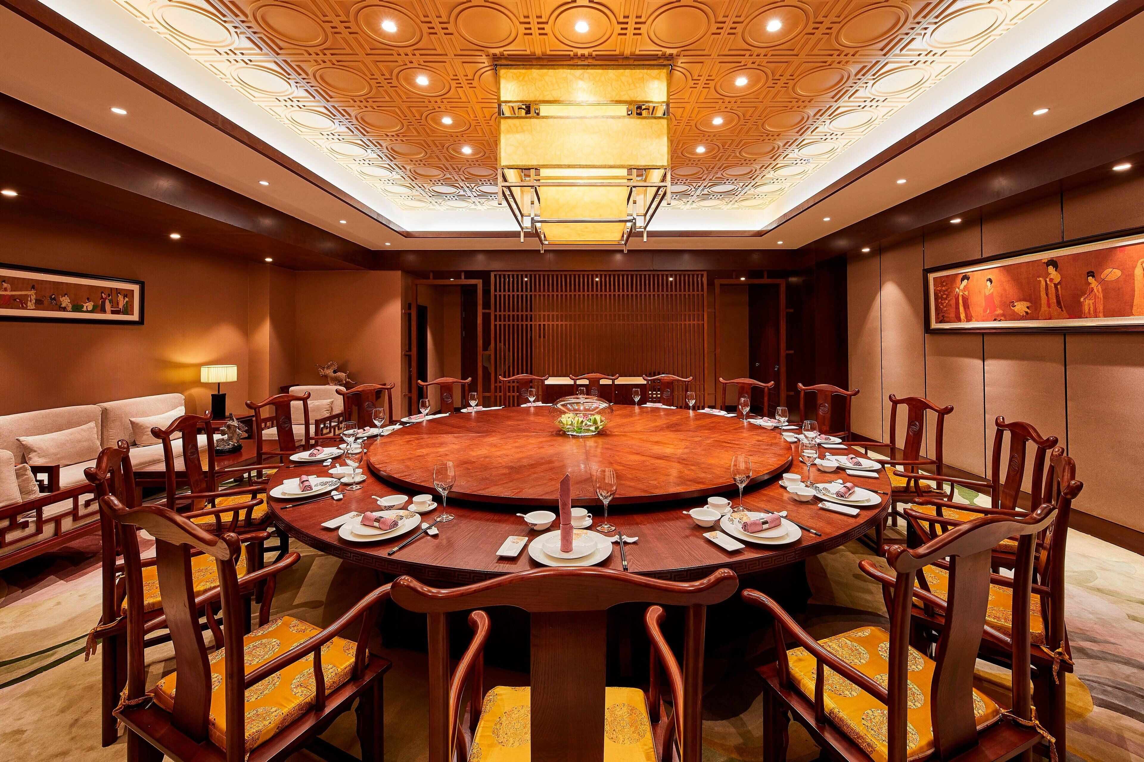 A conference room with a round table, wooden chairs, and a chandelier.