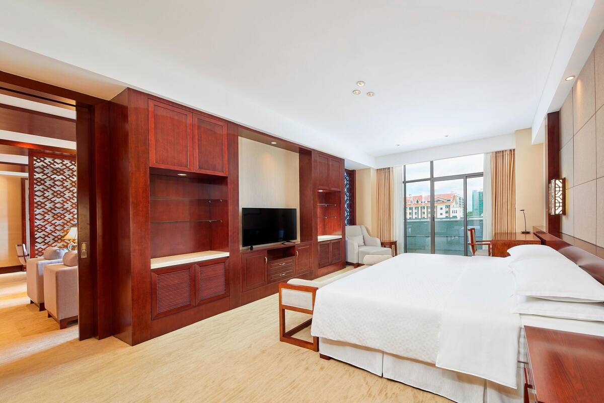 Ein modernes Hotelzimmer mit einem großen Bett, einem Holzschrank, einem Fernseher und Blick auf die Stadt.