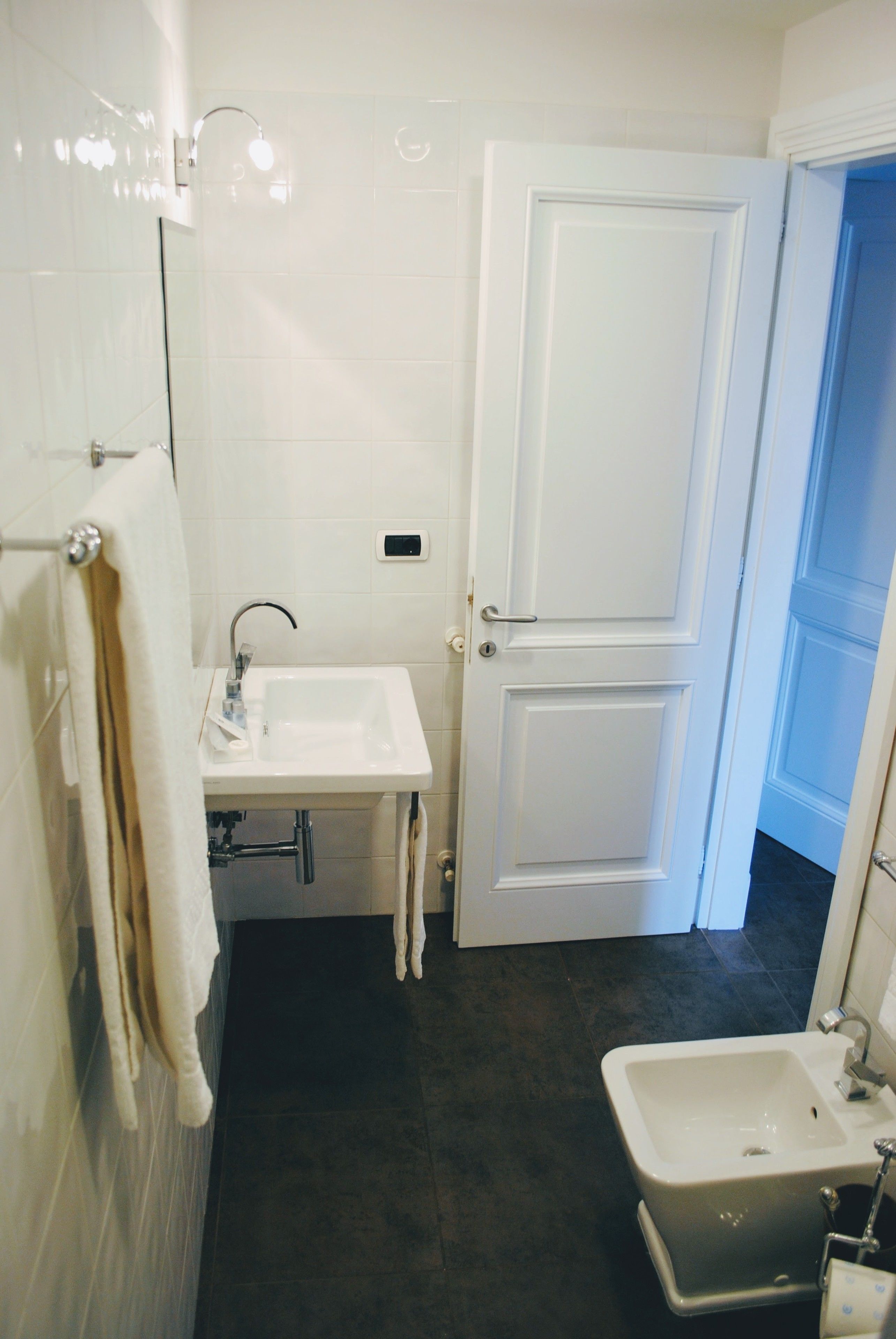A bathroom with a white sink, a small mirror, a towel rack, and a door.