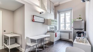 A modern kitchen with white cabinetry, a dining area with a white table and chairs, and a window providing natural light. - Guest House Cavour 278 (Rome)