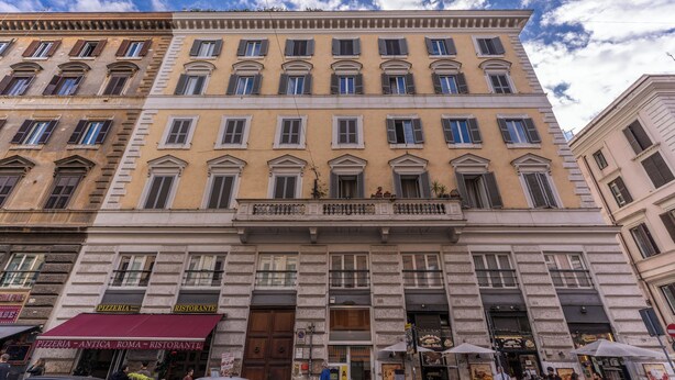 A multi-story building with a classic architectural style, featuring a central entrance with a large wooden door, multiple windows with shutters, and a red awning above a pizzeria. - Guest House Cavour 278 (Rome)