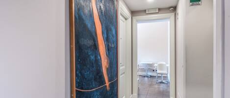 Corredor com uma grande pintura abstrata, uma porta branca e uma placa indicando saída de emergência.
