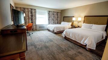 A hotel room with two beds, a desk with a TV, a chair, and a window with curtains.