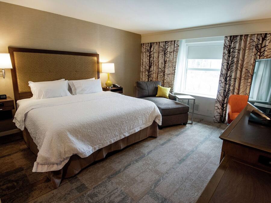 A hotel room with a large bed, a desk, a chair, a TV, and a window with curtains.