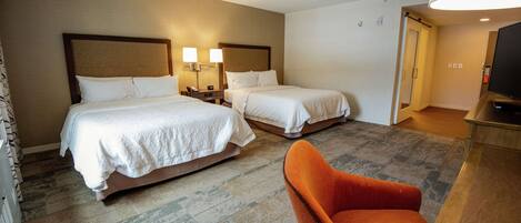 Ein Hotelzimmer mit zwei Betten, einem Fernseher, einem Schreibtisch und einem Sessel.