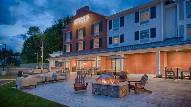 A two-story building with a patio area featuring outdoor seating and a stone fire pit.