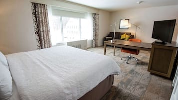 Ein Hotelzimmer mit einem großen Bett, einem Schreibtisch mit Stuhl, einem Fernseher und einem Fenster mit Vorhängen.