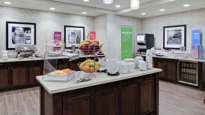 A breakfast bar with various food items and beverages, a coffee machine, and a refrigerator.
