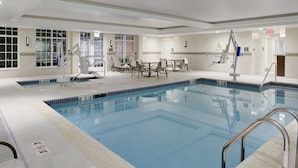 A swimming pool with a lifeguard chair, pool lift, and a seating area with chairs and tables.