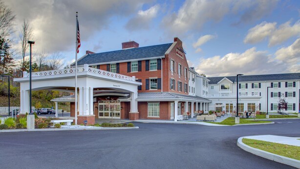 A hotel with a covered entrance, a flagpole with an American flag, and a brick building with multiple windows.