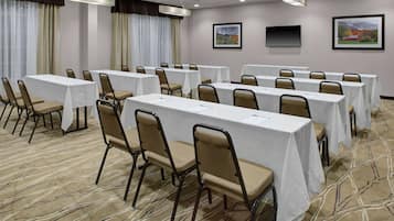 A conference room with multiple tables and chairs, large windows with curtains, and framed pictures on the walls.