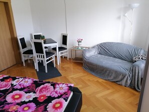 A room with a grey sofa, a white table with chairs, a small side table with a vase of flowers, and a floor lamp. - Cozy Apartment Near Ski (Muldenhammer)