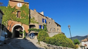 A historic stone building with a clock tower, a bell, and a cobblestone street leading to an archway. - Mansion in Vaison-la-Romaine with Private Pool (Vaison la Romaine)