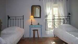 A room with two beds, a small table with a lamp, a mirror, and a window with curtains.