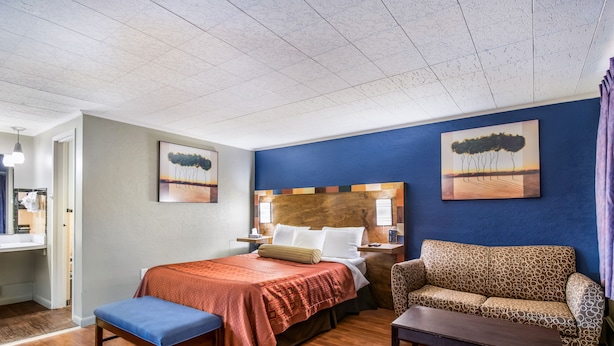 Una habitación de hotel con cama, sofá, banco y obras de arte en las paredes.