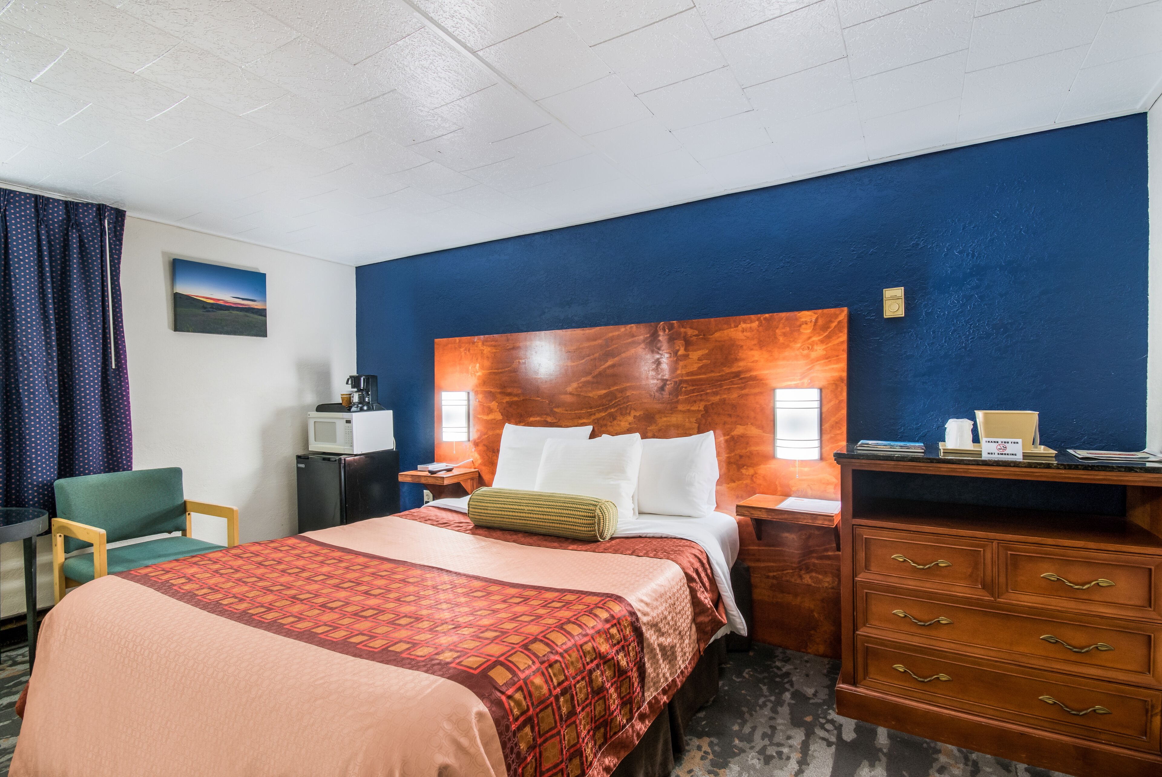 Ein Hotelzimmer mit einem großen Bett, einem Holzkopfschild, einem Schreibtisch, einem Stuhl und einer Kommode.