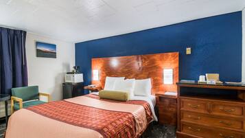 Quarto de hotel com uma cama grande, cabeceira de madeira, escrivaninha, cadeira e cômoda.