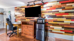 Una cocina moderna con un panel de pared de madera, un televisor de pantalla plana, un refrigerador, un escritorio de madera y una silla de oficina negra.