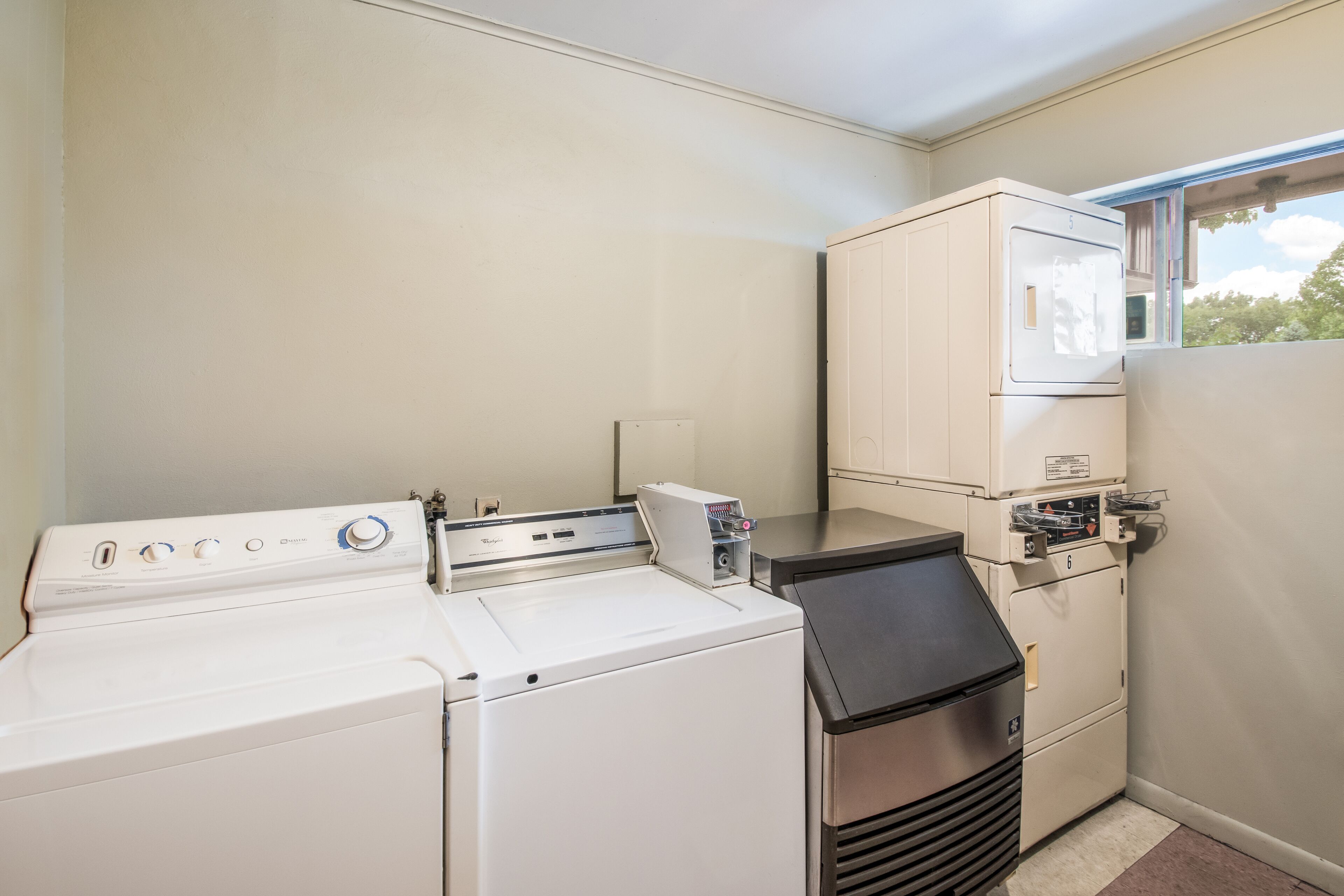 A laundry room with a front-loading washer, a stacked dryer, and a window.