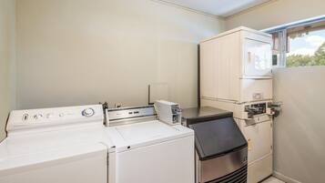 A laundry room with a front-loading washer, a stacked dryer, and a window.