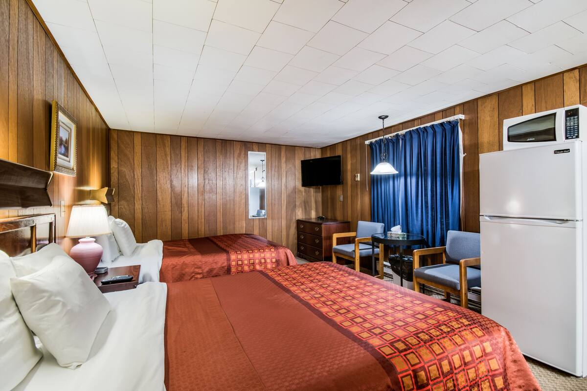 A hotel room with two beds, a desk with a chair, a television, and a refrigerator.