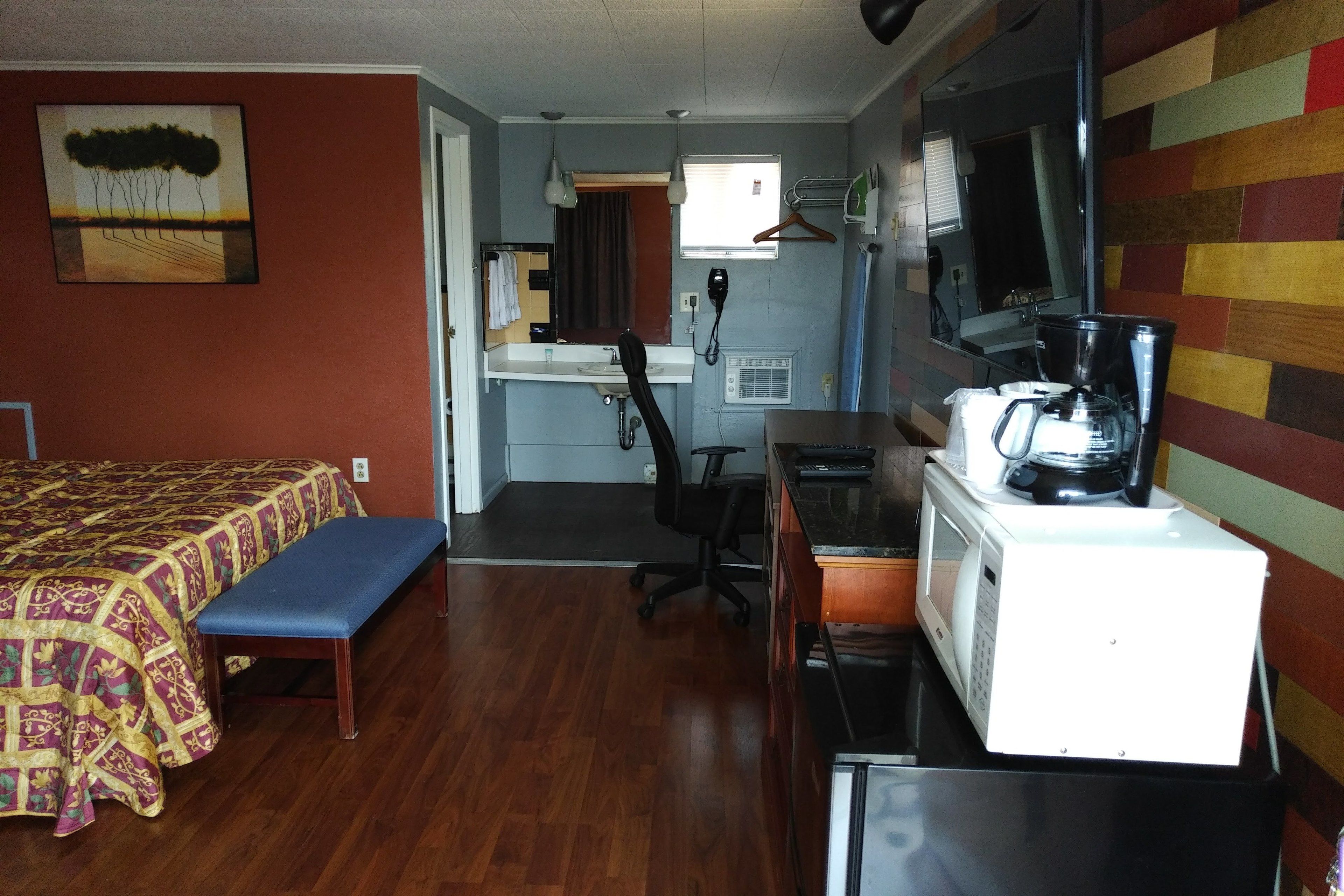 Une chambre d’hôtel compacte comprenant un lit, une banquette, un bureau avec une machine à café, un micro-ondes et une petite kitchenette.